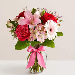 Bouquet of red roses, pink lilies, and a white gerbera daisy in a glass vase