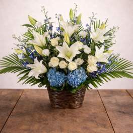 White lilies, roses, and blue hydrangeas in a wicker basket