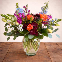 Mixed bouquet of orange, purple, and blue flowers in a clear glass vase