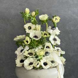 White anemone arrangement in a round gray container with a ribbon