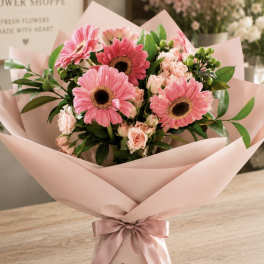 Pink gerbera daisy and rose bouquet wrapped in blush paper with a ribbon