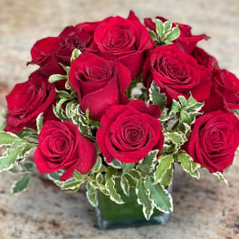Red roses arranged in a clear glass vase with variegated greenery
