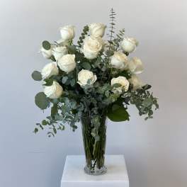 White roses arranged in a tall glass vase with eucalyptus foliage