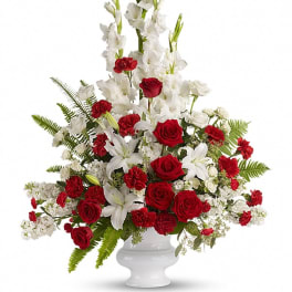 Tall red and white sympathy arrangement with roses, carnations, lilies, and gladiolus in a white pedestal vase