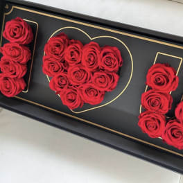 Red roses arranged in a black box with gold heart and letter outlines