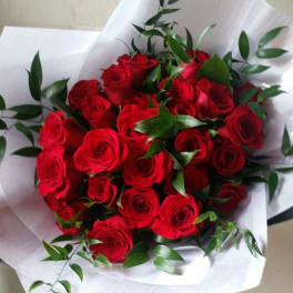 Bouquet of red roses wrapped in white paper with green foliage
