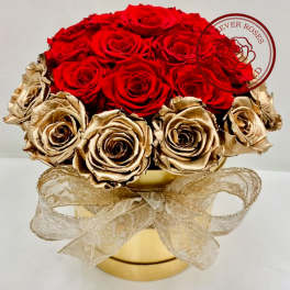 Red and gold roses arranged in a round gold box with a sheer ribbon bow.