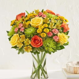 Mixed bouquet of yellow, orange, and pink flowers in a clear glass vase