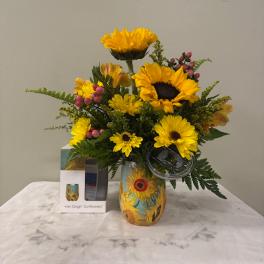 Sunflower arrangement in a painted vase with a gift box beside it