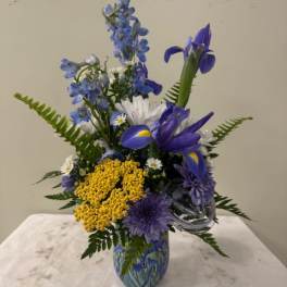 Blue and yellow mixed flower arrangement in a glass vase