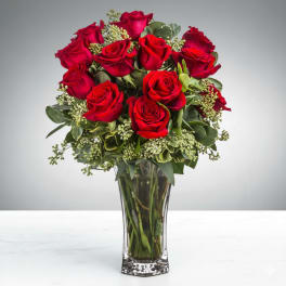 Red roses arranged in a clear glass vase with greenery