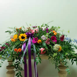 Large colorful floral casket spray with ribbon on a table