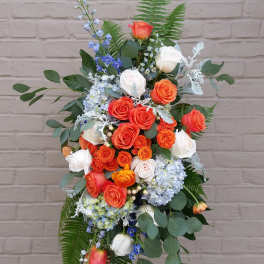 Tall floral spray with orange and white roses and blue flowers on a stand