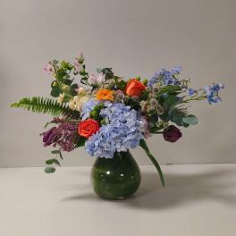 Mixed bouquet in a green glass vase with blue hydrangeas and orange roses