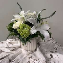 White lilies and roses arranged in a white vase with green accents