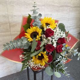 Bouquet of red roses and yellow sunflowers with white filler in red wrap