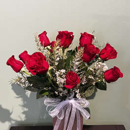 Red roses arranged in a pink vase with a sheer ribbon bow
