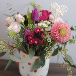 Mixed pink and purple flower arrangement in a heart-patterned mug