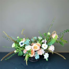 Low floral arrangement with peach and white roses in a black container