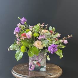 Mixed bouquet in a square glass vase with purple, pink, and green blooms