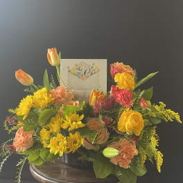 Mixed bouquet in a low container with yellow, orange, and pink flowers