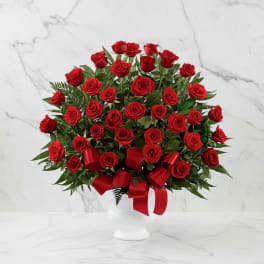 Red roses arranged in a white vase with a red ribbon