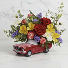 Red roses and mixed flowers arranged in a red toy car container