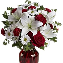 Bouquet of red roses, white lilies, and daisies in a red glass vase