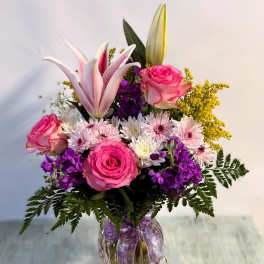 Bouquet of pink roses, lilies, and purple flowers in a glass vase