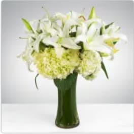 Tall glass vase of white lilies and pale green hydrangeas in a compact, all-around arrangement