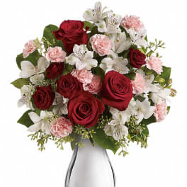 Arrangement of red roses, white alstroemeria, and light pink carnations in a shiny silver vase