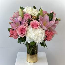Pink roses and lilies arranged with white hydrangeas in a glass vase.