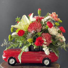 Floral arrangement in a red toy car with lilies and carnations