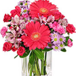 Pink gerbera daisies, roses, and purple daisies in a clear square vase