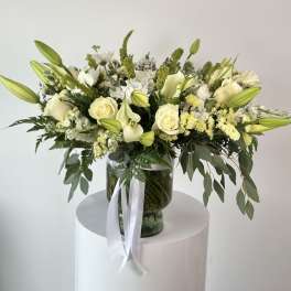 White floral arrangement in a glass vase with a white ribbon