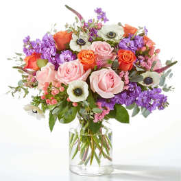 Mixed bouquet of pink and orange roses with purple flowers in a glass vase