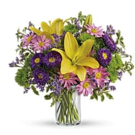 Yellow lilies and purple daisies in a clear glass vase