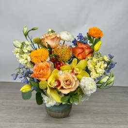 Mixed bouquet of orange, yellow, white, and blue flowers in a ceramic vase