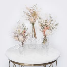 Three dried floral arrangements in clear glass vases on a round table