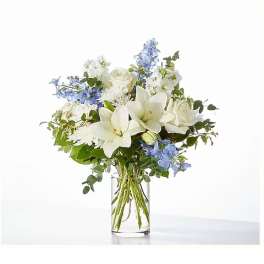 White lilies and roses with blue flowers in a clear glass vase