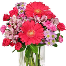 Pink gerbera daisies, roses, and purple daisies in a clear glass vase