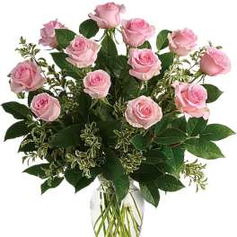 Pink roses arranged in a clear glass vase with mixed greenery