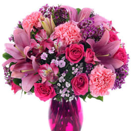 Pink bouquet of lilies, roses, and carnations arranged in a bright pink glass vase