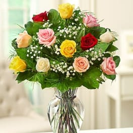 Mixed-color rose bouquet with white filler blooms arranged in a clear glass vase