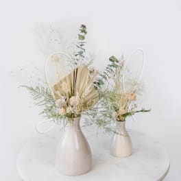 Two dried floral arrangements in cream vases on a round table