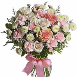 Pink and white rose bouquet in a glass vase with a pink ribbon