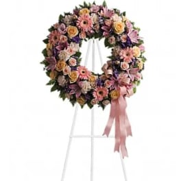 Pastel floral wreath on a white stand with a pink ribbon