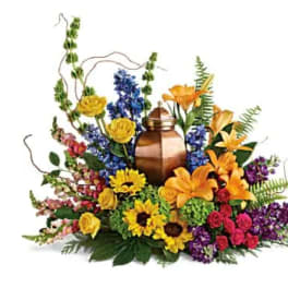 Mixed floral arrangement around a copper urn with yellow, orange, purple, and red blooms
