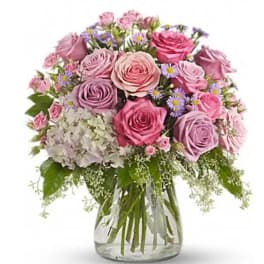 Pink and lavender roses in a clear glass vase with small purple daisies
