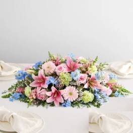 Low floral centerpiece with pink lilies, roses, and blue flowers on a white table